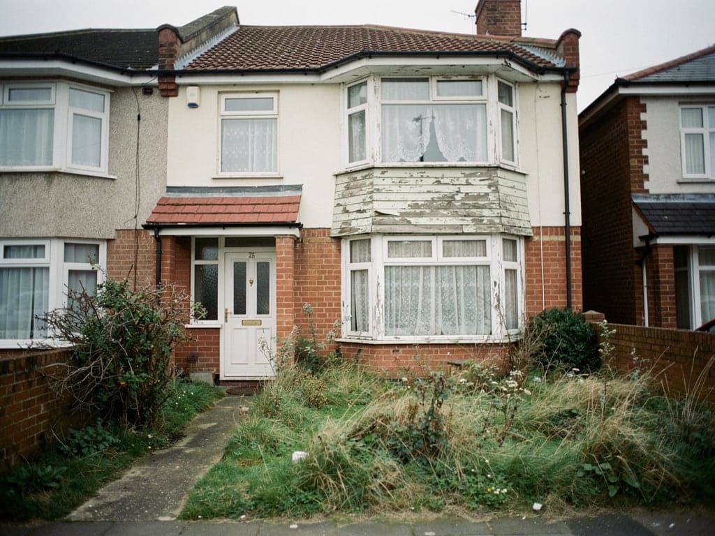 An empty 1930s semi detached house with an overgrown front garden